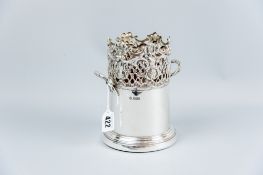 A wooden based silver wine bottle holder with twin handles and the top third having a latticed and