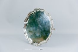 A silver decanter tray having a wide wavy border, uninscribed on three hoof supports, 31 cms diam,