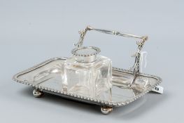 An oblong silver inkstand with feather edged border and with a centre plain square glass bottle