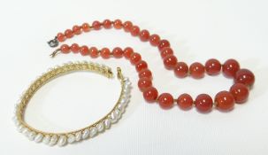 A strand of graduated red amber beads, 36cms long; together with a yellow metal bracelet of 43