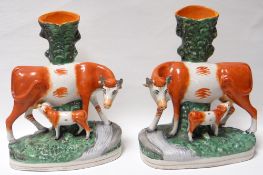 A pair of Staffordshire red and white cow and suckling calf spill-holders on grass-effect oval bases