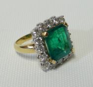 An emerald and diamond cluster 18ct yellow gold ring, the emerald being 8.6ct approx and of step cut
