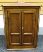 An oak hanging two-door corner cupboard, with two shaped shelves to the interior, 101cms high, circa