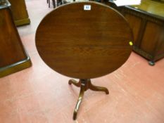 An antique oak tilt top table on turned column tripod base (legs reduced), 60 cms diam top