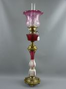 A Victorian oil lamp with circular embossed brass base on four brass feet, white overlay and ruby
