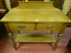 An early 20th Century oak side table having two drawers with brass drop handles to turned, cup and