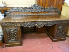 A late 19th/early 20th Century carved oak kneehole sideboard, the rail back heavily carved with a