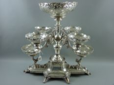 An extremely impressive all silver table centrepiece having a curved square centre base with