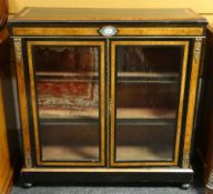A two-door ebony and walnut bookcase, ormolu mounted and with oval floral painted porcelain