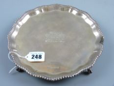 A circular silver letter tray with feather edged border on four ball and claw supports with