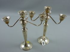 A pair of circular based twin branch single sterling silver candelabra, the bases having gadrooned