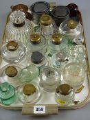 Approximately eighteen glass circular based inkwells, mostly with lids, a bronze example and two
