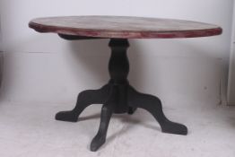 A large shabby chic painted dining table raised on a tripod base with large oval table top above.