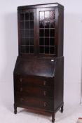 A 1930's oak Bureau bookcase having lead lined coloured glass doors top over four straight drawers.
