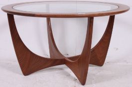 A 1970's retro g-plan teak wood atomic style circular glass coffee table raised on angled supports