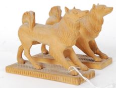 A pair of 20th century Inuit carved wooden figures of dogs / wolves being raised on wooden plinths.