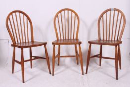 A set of 3 Ercol stick back kitchen dining chairs raised on tapered supports united by stretchers.