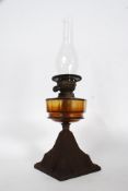 A 19th century cast metal oil lamp having an amber glass reservoir over tapered pierced base with