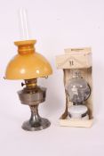 A vintage orange glass shaded oil lamp, along with another contemporary lamp within a box.