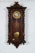 A Victorian 19th century wall clock with enamel face and carved wooden finials atop the case.