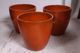 A collection of 3 contemporary orange glazed large flower pots