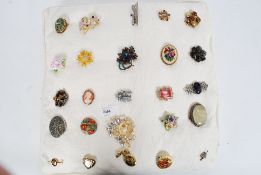 A collection of 25 costume jewellery and silver brooches all mounted on a pad