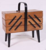 A 1950's beech and ebonised metamorphic sewing box having sectional extending body with handle to