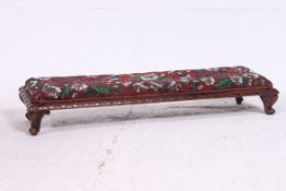 A Victorian walnut long fender stool raised on cabriole supports with a carved apron having