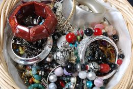 A basket of assorted costume jewellery to include bangles, necklaces and other items.