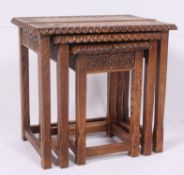 A Jacobean style carved oak nest of tables being raised on squared legs with stretchers having