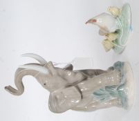 A Nao figurine model of an elephant with raised foot and trunk set on a naturalistic plinth base.