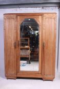 A 1930's Art Deco oak triple wardrobe armoire having central mirror door with shelved and hanging