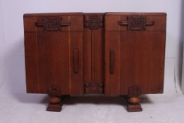A 1930's oak sideboard raised on staggered feet with twin doors astride drawers with carved detail