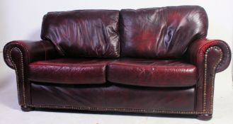A two seat Victorian Chesterfield style sofa settee in oxblood red leather finished with brass