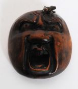A 20th century Japanese wooden buddha face Netsuke type carving with unusual applied bronze fly