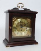 A 20th century mantel clock in mahogany with brass features and brass handle to top.