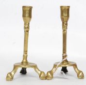A pair of brass candlesticks raised on tripod bases, medieval style with single sconces atop.