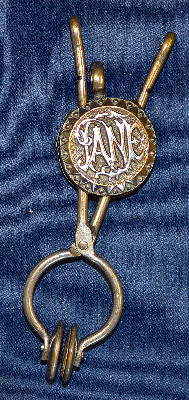 Silver plated brass tennis skirt lifter with a rounded centre piece and a raised design showing'