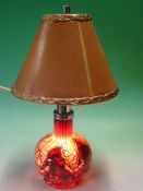 Monart Glass. A table lamp, the base in shades of red and black with flecks of yellow, illuminated