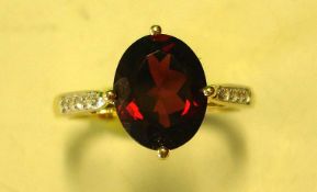 A Garnet Solitaire Ring With an oval stone and four diamonds to each shoulder. In gold marked 375.