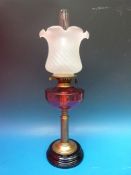 A large brass oil lamp with cranberry glass bowl and opalescent shade