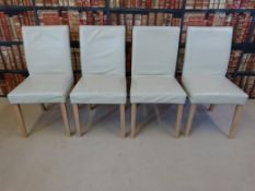 A set of four cream leatherette and beech dining chairs