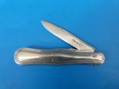 A white metal folding fruit knife with fold out blade and pick, the body with shaped edge and