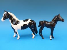 A Beswick piebald pinto pony together with a Beswick black foal with white legs