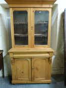 A Victorian pine bookcase/display cabinet, the top with arched topped glazed doors with two shelves,