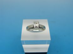 A white metal ring set with a emerald cut diamond solitaire measuring approximately 0.
