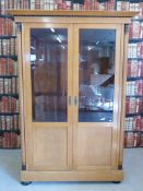 A Biedermeier satinwood and ebonised cabinet having part glazed doors flanked by columns