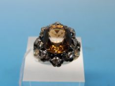 A yellow metal ring set with a dark orange quartz surrounded by diamonds in a platinum setting