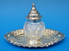 A Victorian hallmarked silver inkwell with cut glass silver-mounted bottle on an embossed tray,