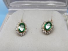 A pair of 18ct gold earrings each set with an oval emerald surrounded by diamonds